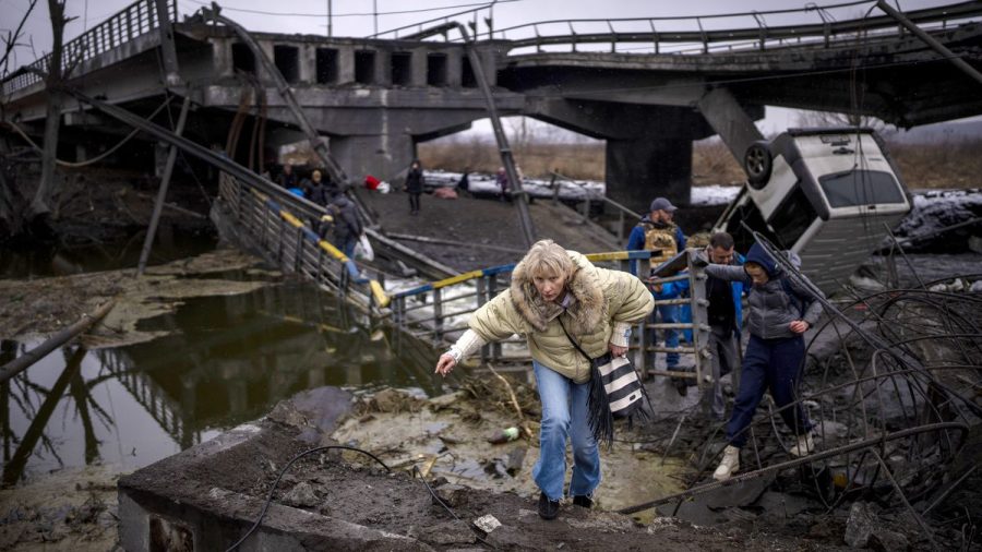 A women flees with her family across a destroyed bridge in the outskirts of Kyiv